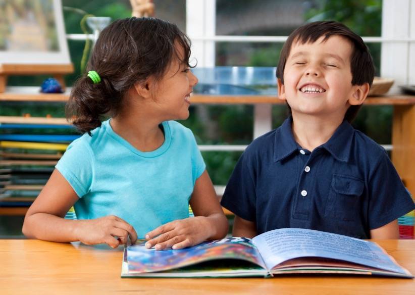 two students laughing while reading a book