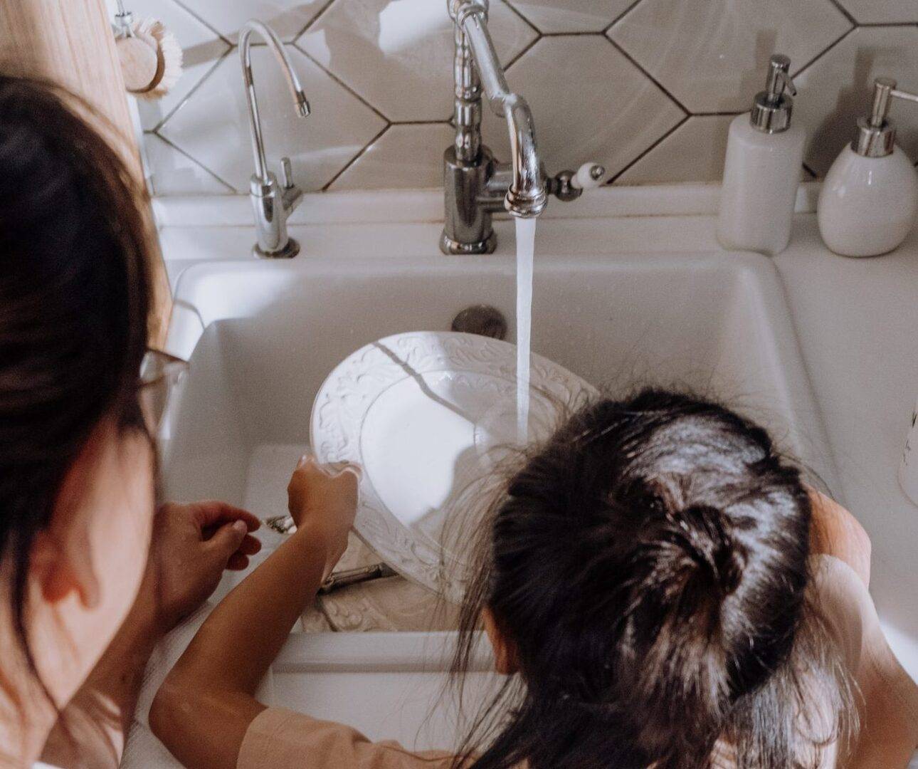 child washing dished with help from an adult