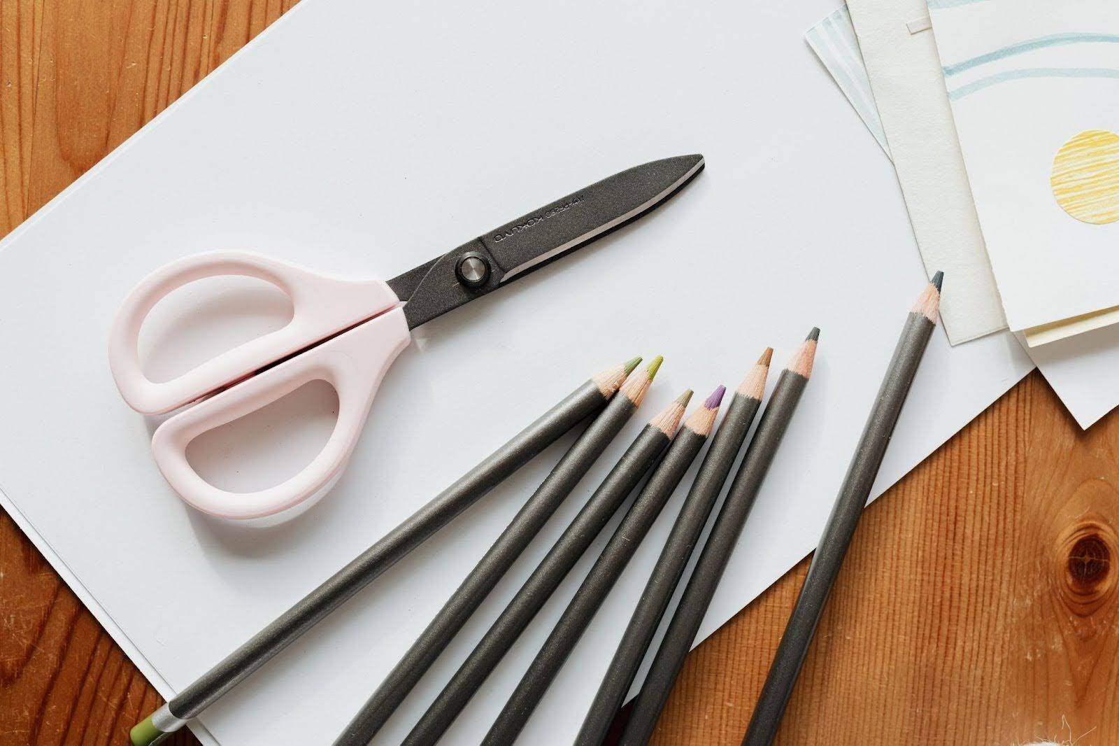 close up of desk covered with colored pencils, paper, and a pair of scissors.