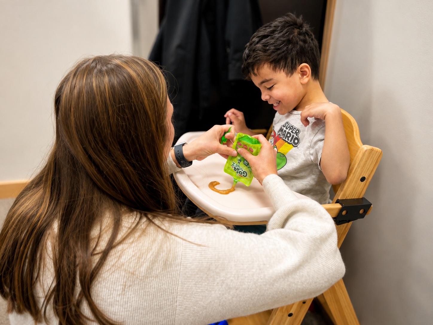 Therapist helping young boy in a high chair open a fruit pouch during a feeding therapy session