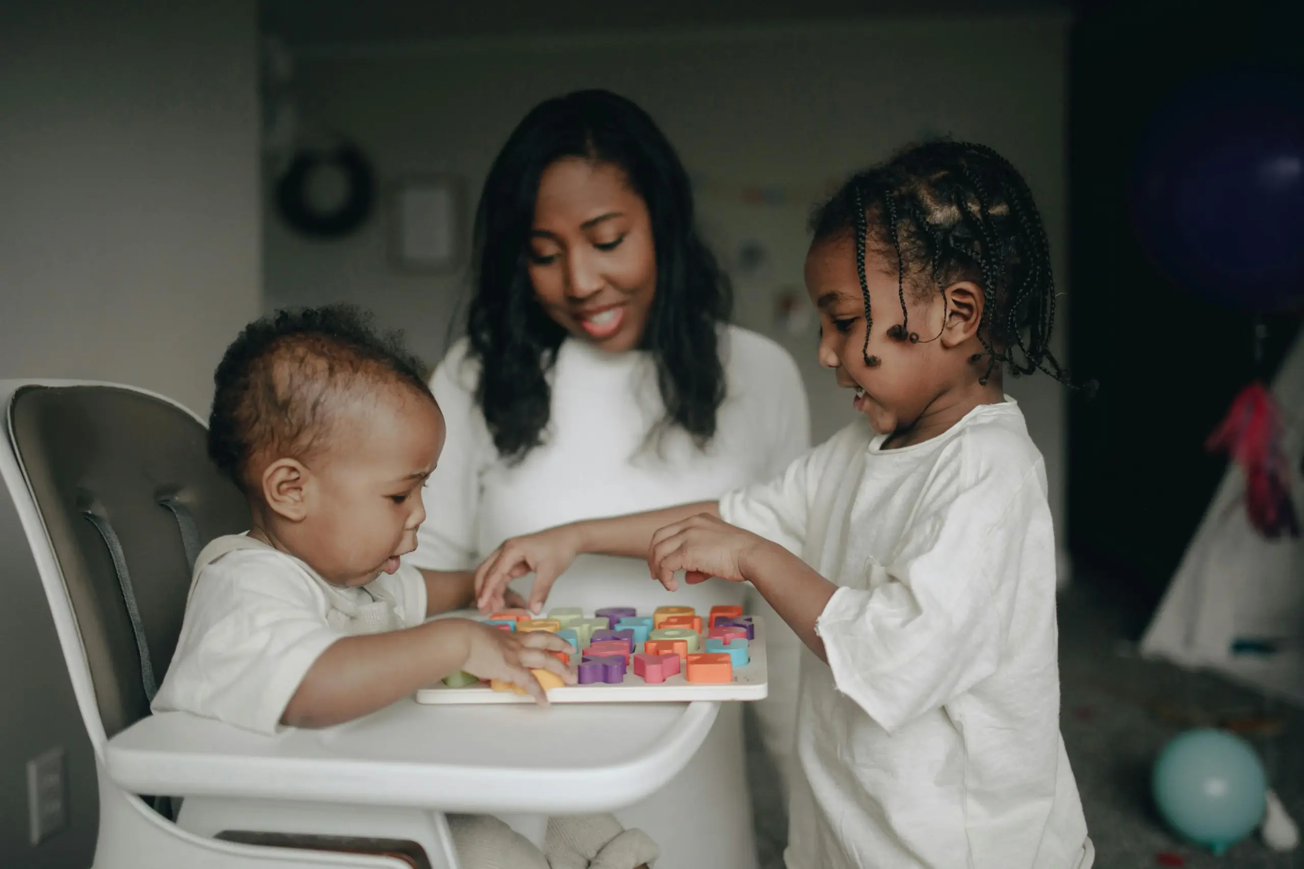 baby sits in high chair while toddler and mother play on high chair top together