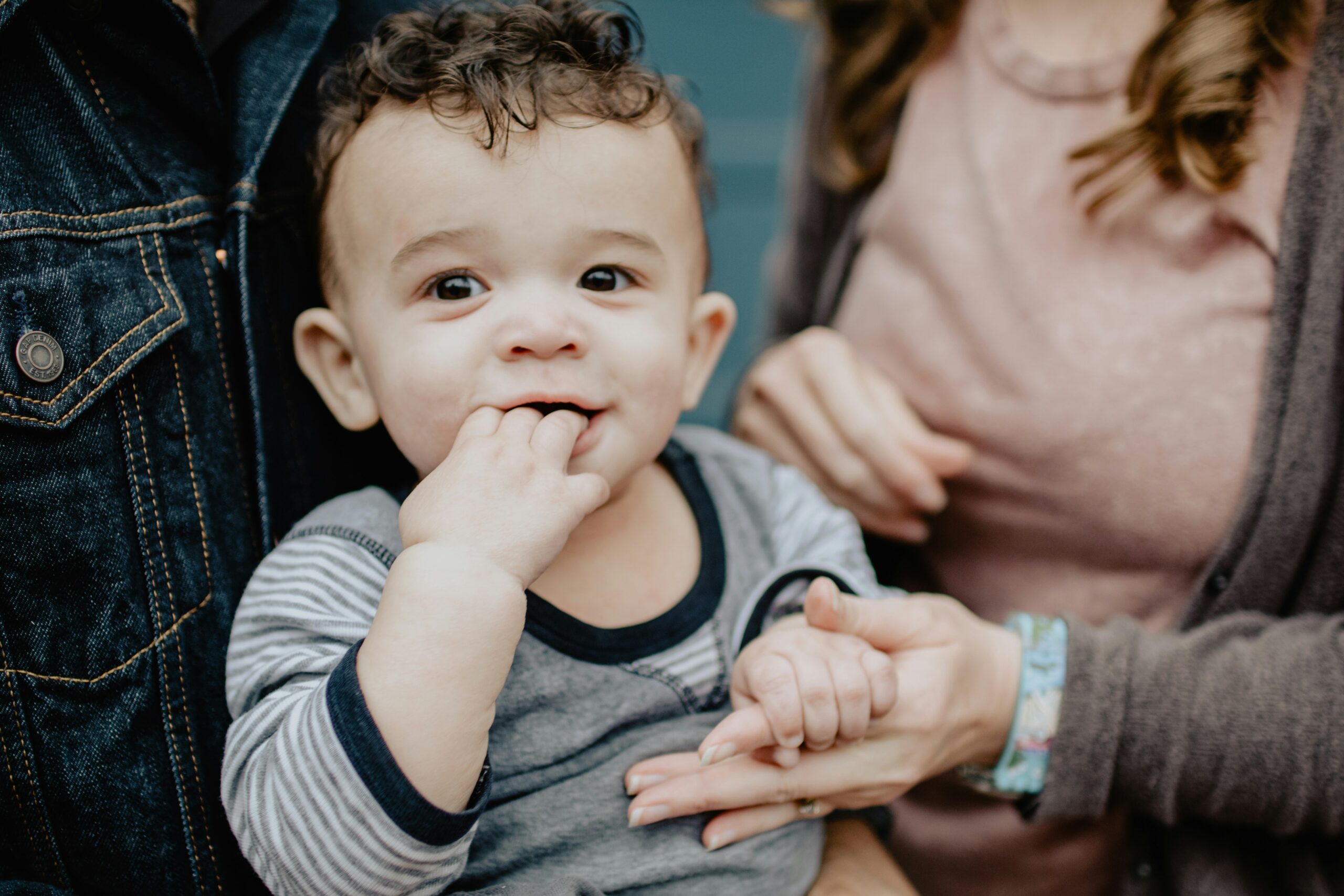 toddler held by a parent has his hand in his mouth, smiling