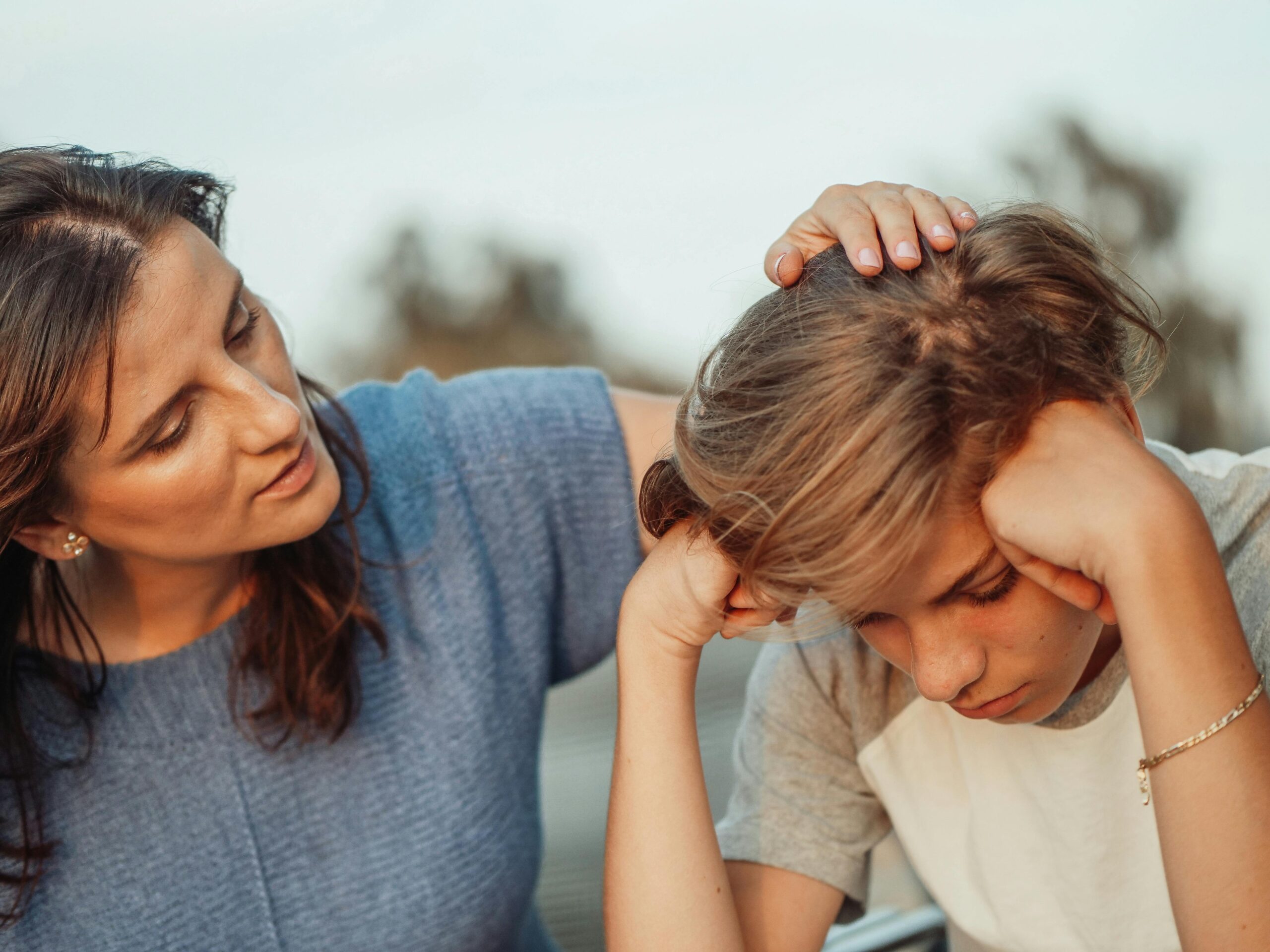 boy holds his head in his hands as mom consoles him