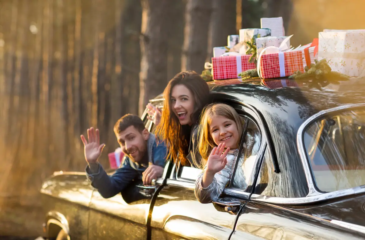 mom, dad and daughter sit in car with presents on it, waving