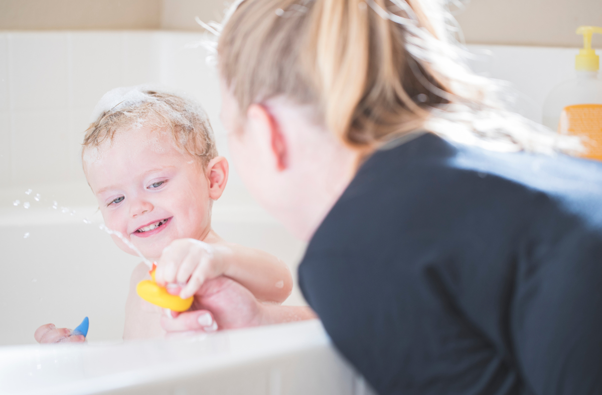 mother watches toddler play in the bathtub