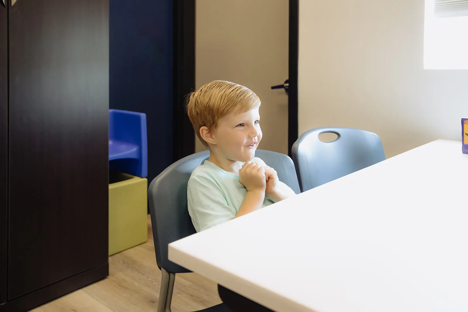 how-to-support-a-child-who-stutters Young boy seated at a table pausing thoughtfully during a fluency therapy session at ETLC